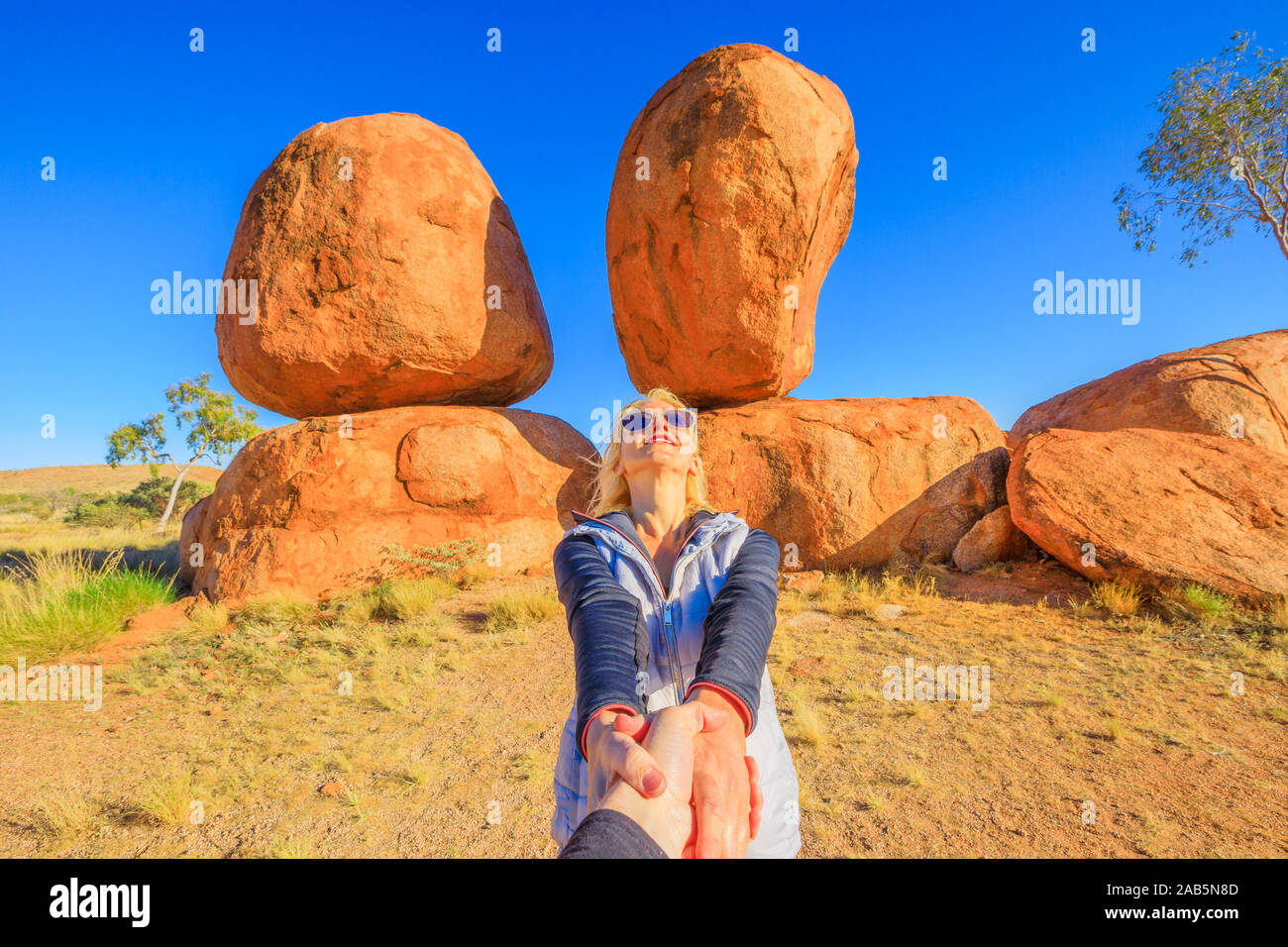 Couple hand in hand at iconic Devils Marbles in Northern Territory: the Eggs of mythical Rainbow Serpent. Follow me, tourist woman at Outback Stock Photo