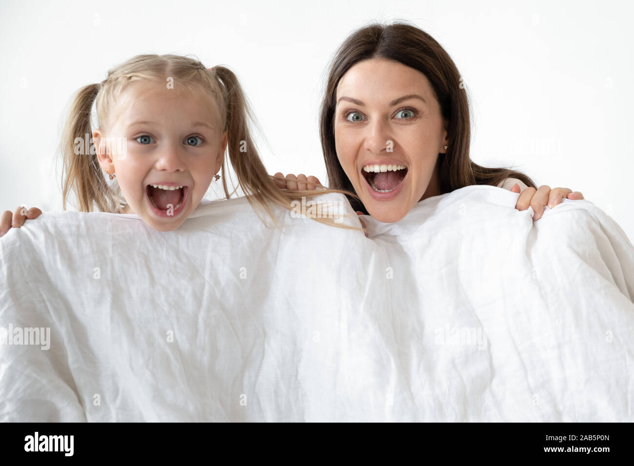 Excited mom and child daughter hold duvet looking at camera Stock Photo