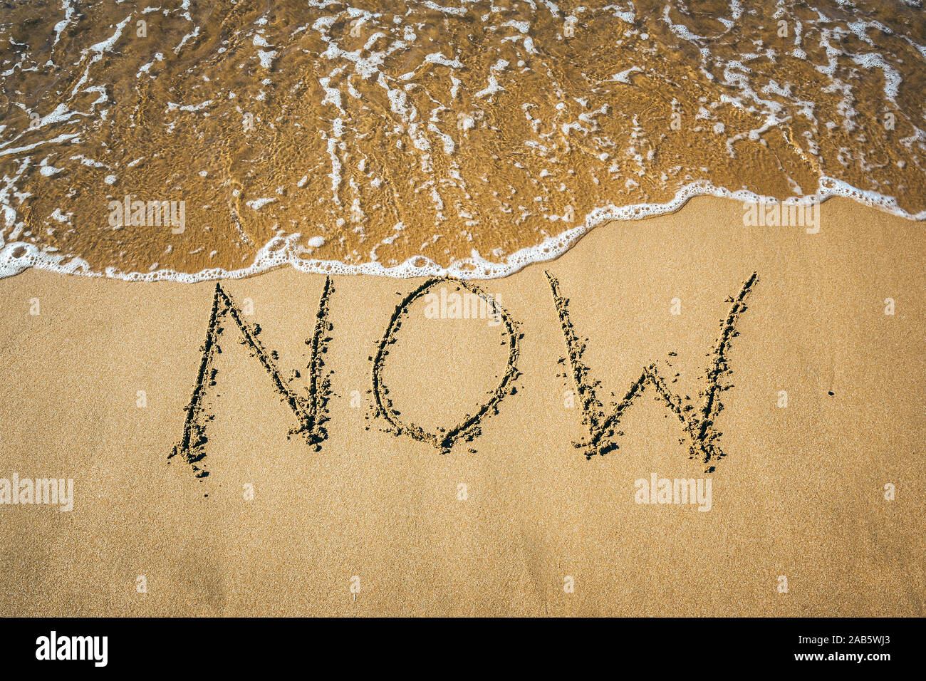 Ein Sandstrand, auf dem 'Now' geschrieben steht. Stock Photo