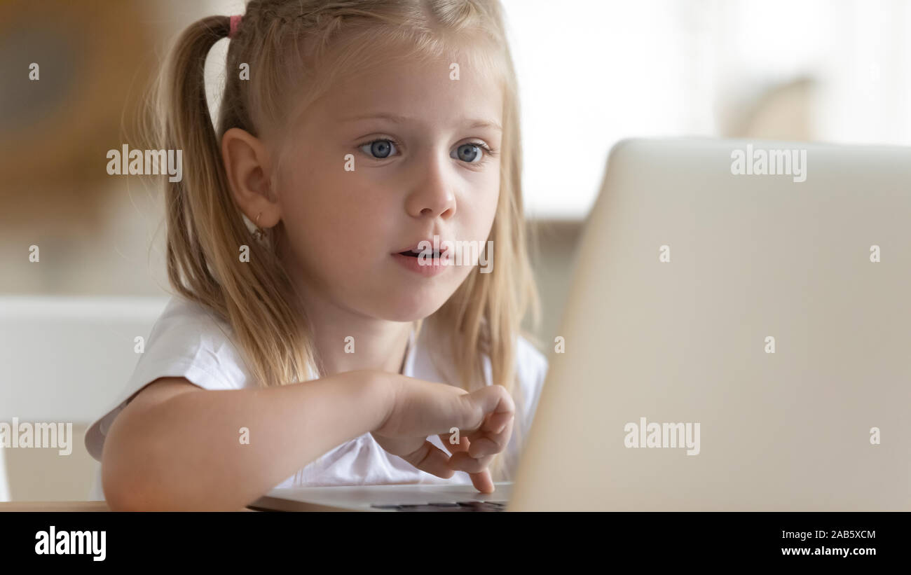 Curious surprised little kid girl using laptop alone at home Stock Photo
