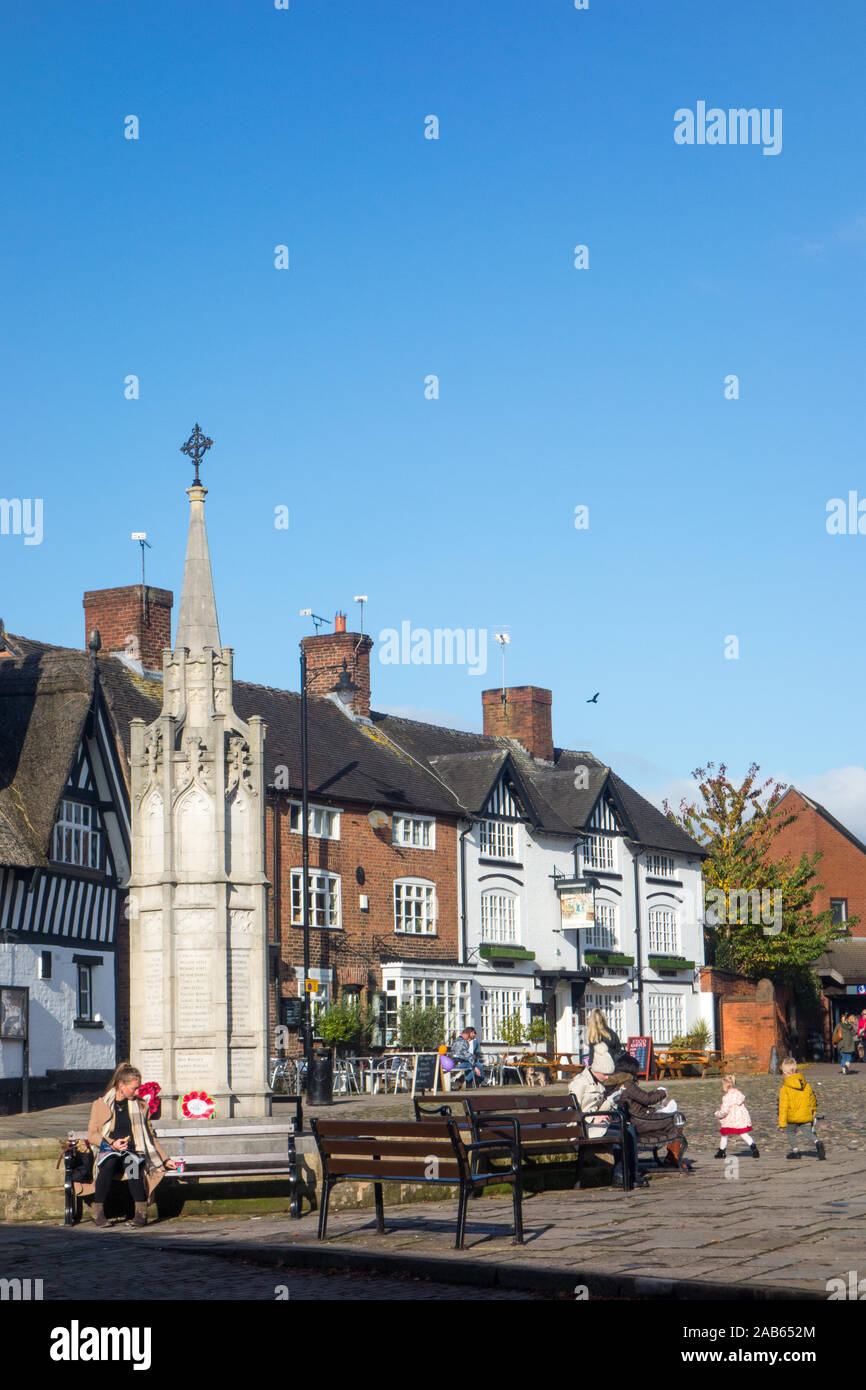 People sitting in the ancient cobbled market square in the Cheshire market town of Sandbach Cheshire  with the the war memorial in the foreground Stock Photo