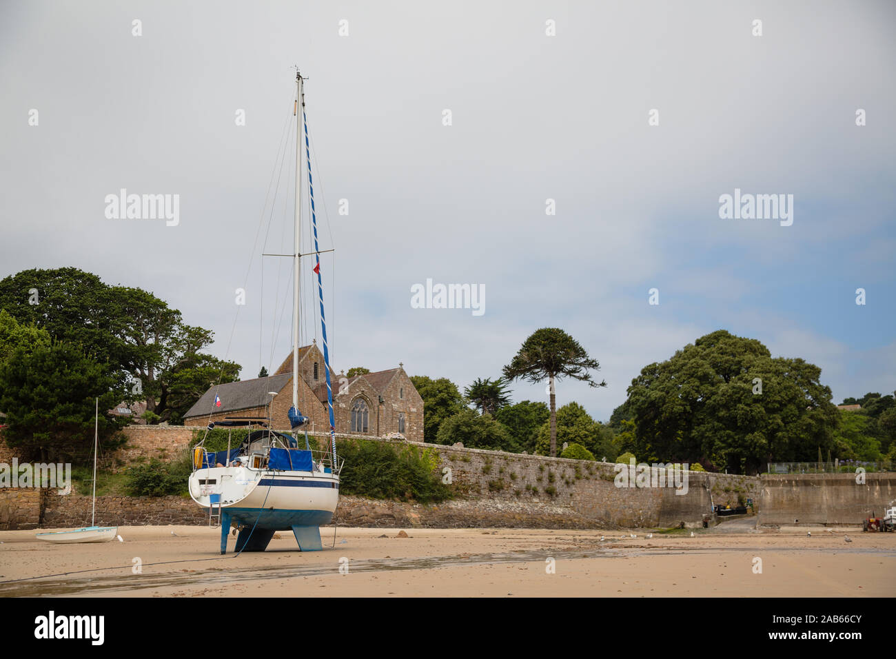 Sailing boat on the beat with church and trees - Jersey Island, Channel Islands Stock Photo