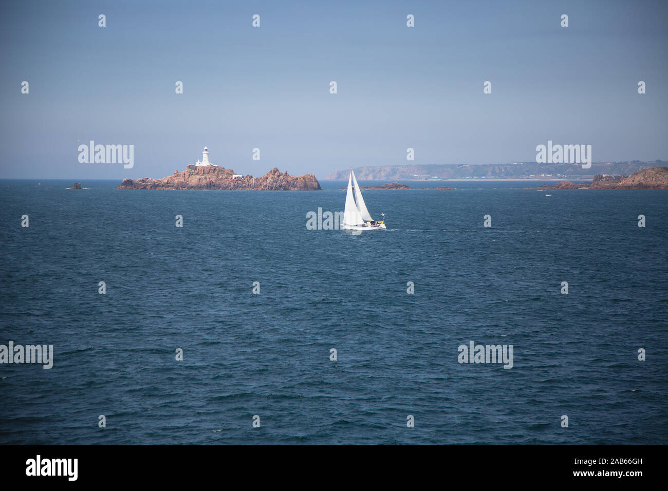Sailing boat off the coast of Guernsey with a light house and rocks - channel islands Stock Photo