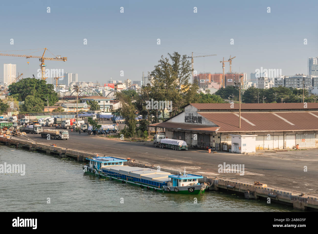 Ho Chi Minh City, Vietnam - March 13, 2019: Downtown port on Song Sai Gon river at sunset. Small modern blue barge at quay near warehouse where truck Stock Photo