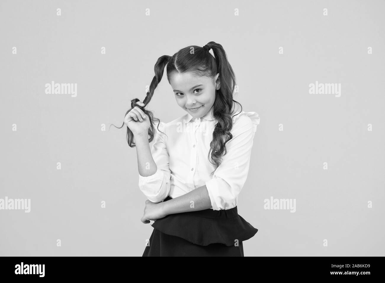 Modest hairstyle. Cute little schoolchild winding hairstyle around her  finger on yellow background. Fashion girl with long ponytail hairstyle in  formal style. Small kid styling hairstyle for school Stock Photo - Alamy