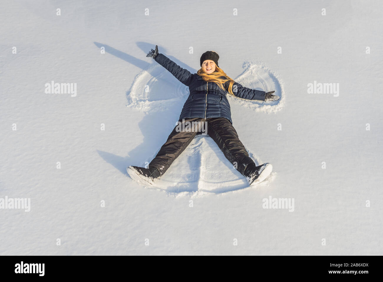 Woman warmly clothed in a cold winter forest makes snow angel figure at park. Copy space text Stock Photo