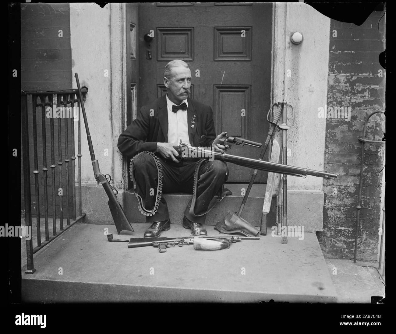 Man sitting on porch with multiple guns and rifles ca. 1927 Stock Photo