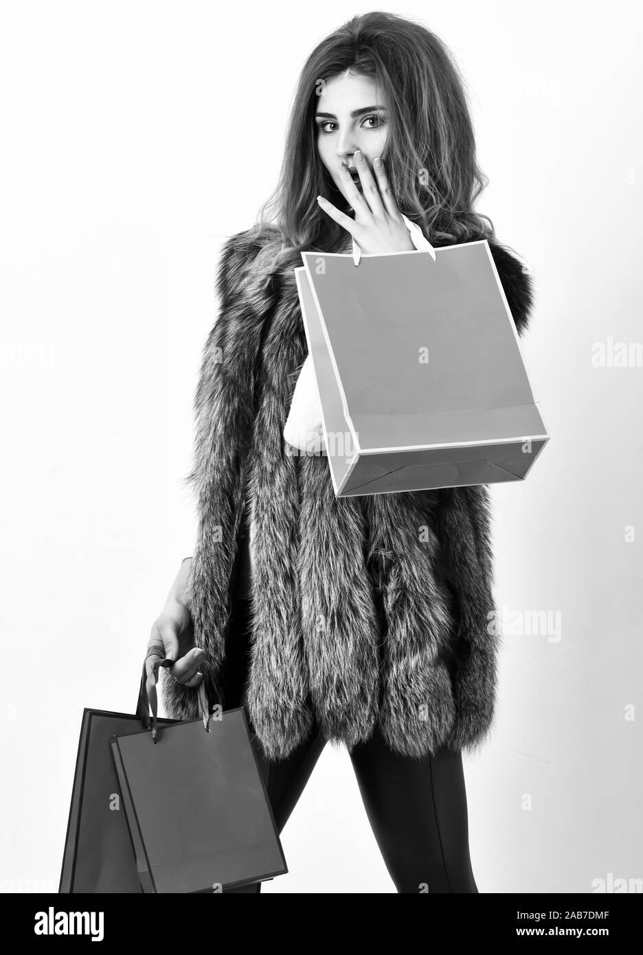 Shopping concept. Woman shopping luxury boutique. Lady hold shopping bags in hands. Fashionista buy fashionable clothes in shop. Girl makeup face long hairstyle wear fur vest white background. Stock Photo