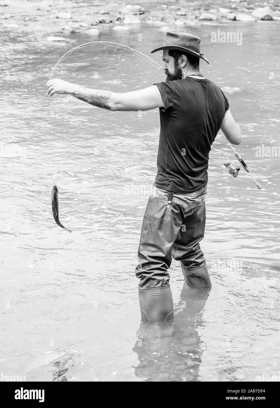Fishing masculine hobby. Brutal man wear rubber boots stand in river water.  Fisher weekend activity. Fisher with fishing equipment. Fish on hook.  Leisure in wild nature. Fun of fishing is catching Stock