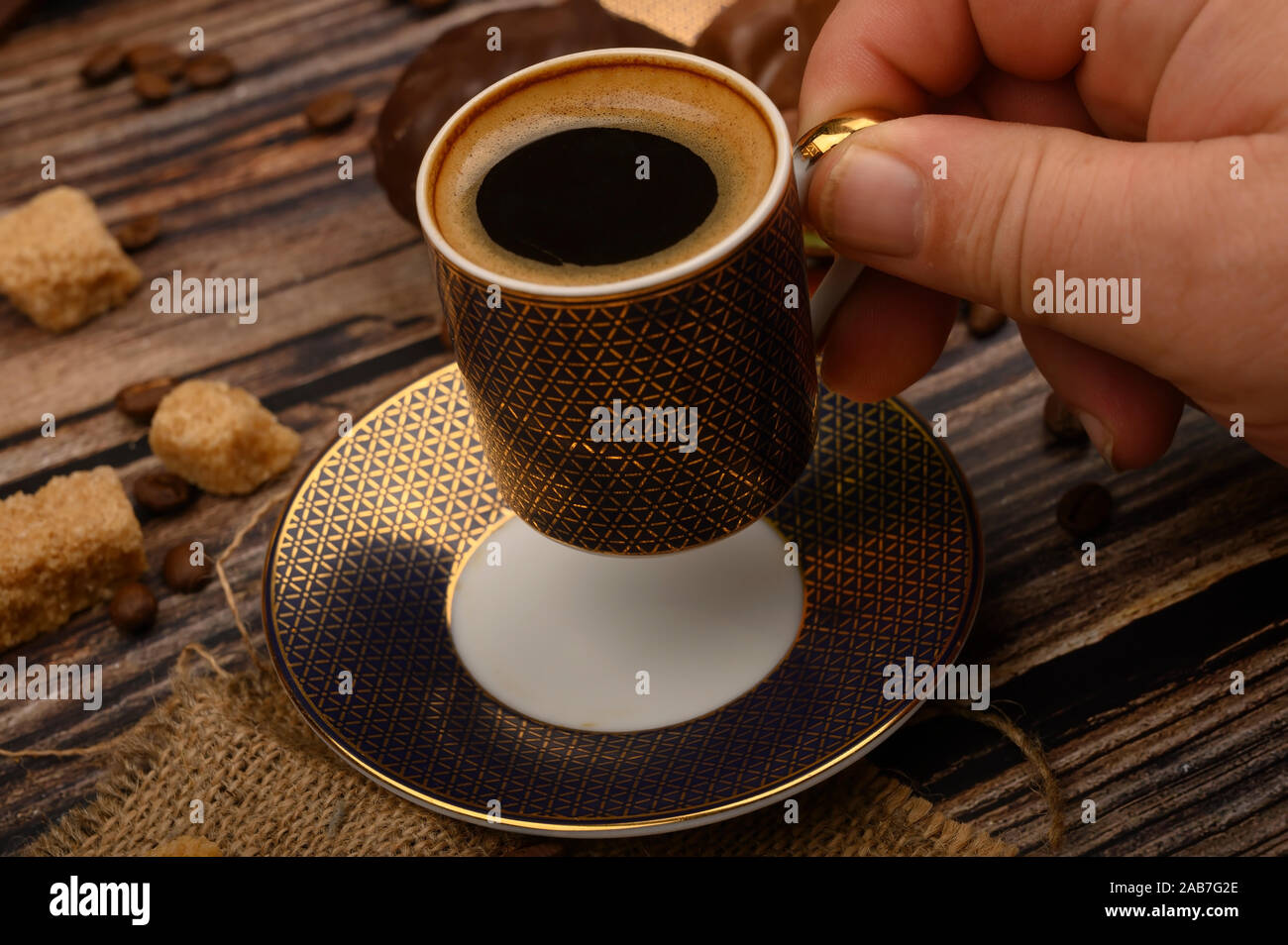 https://c8.alamy.com/comp/2AB7G2E/the-girls-hand-holds-a-cup-of-coffee-over-a-wooden-table-with-brown-sugar-and-coffee-beans-2AB7G2E.jpg