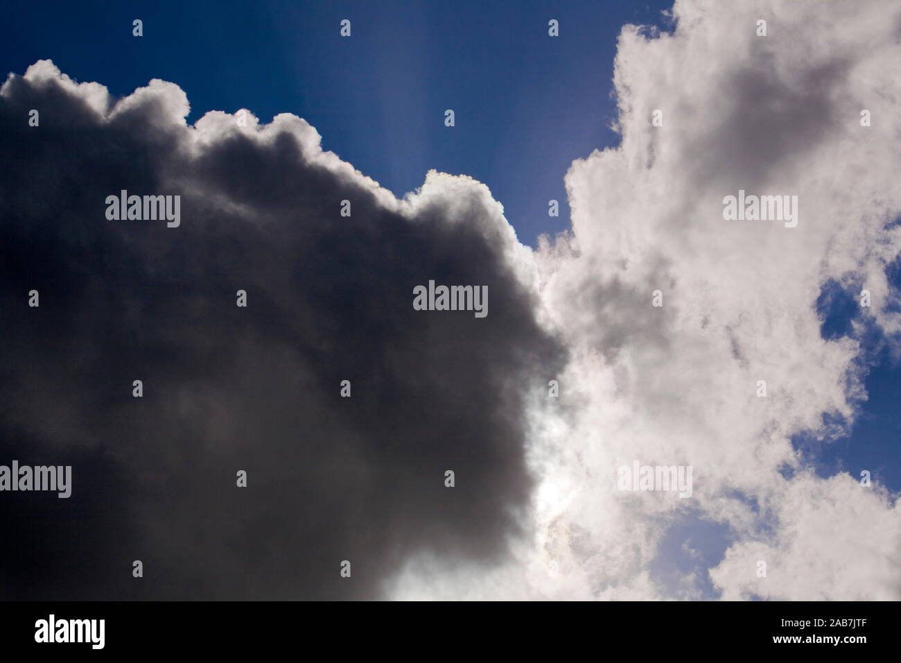 Dunkle Regenwolken und sich auftuermende dichte Quellwolken vor blauem Himmel Stock Photo