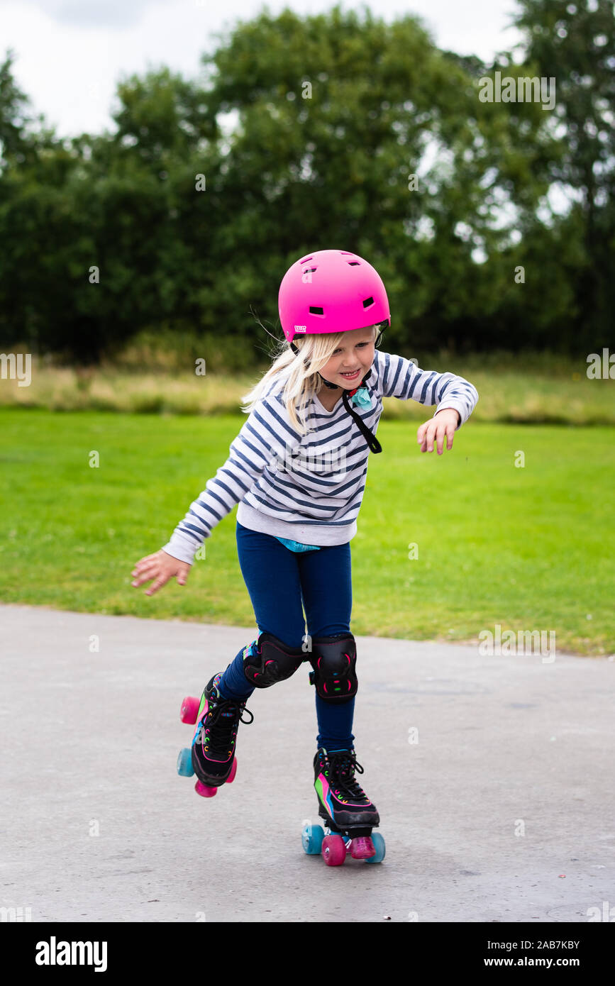 A cute little girl in a pink helmet learning to roller skate at the local  council run skate park in the city, Stoke on Trent Stock Photo - Alamy
