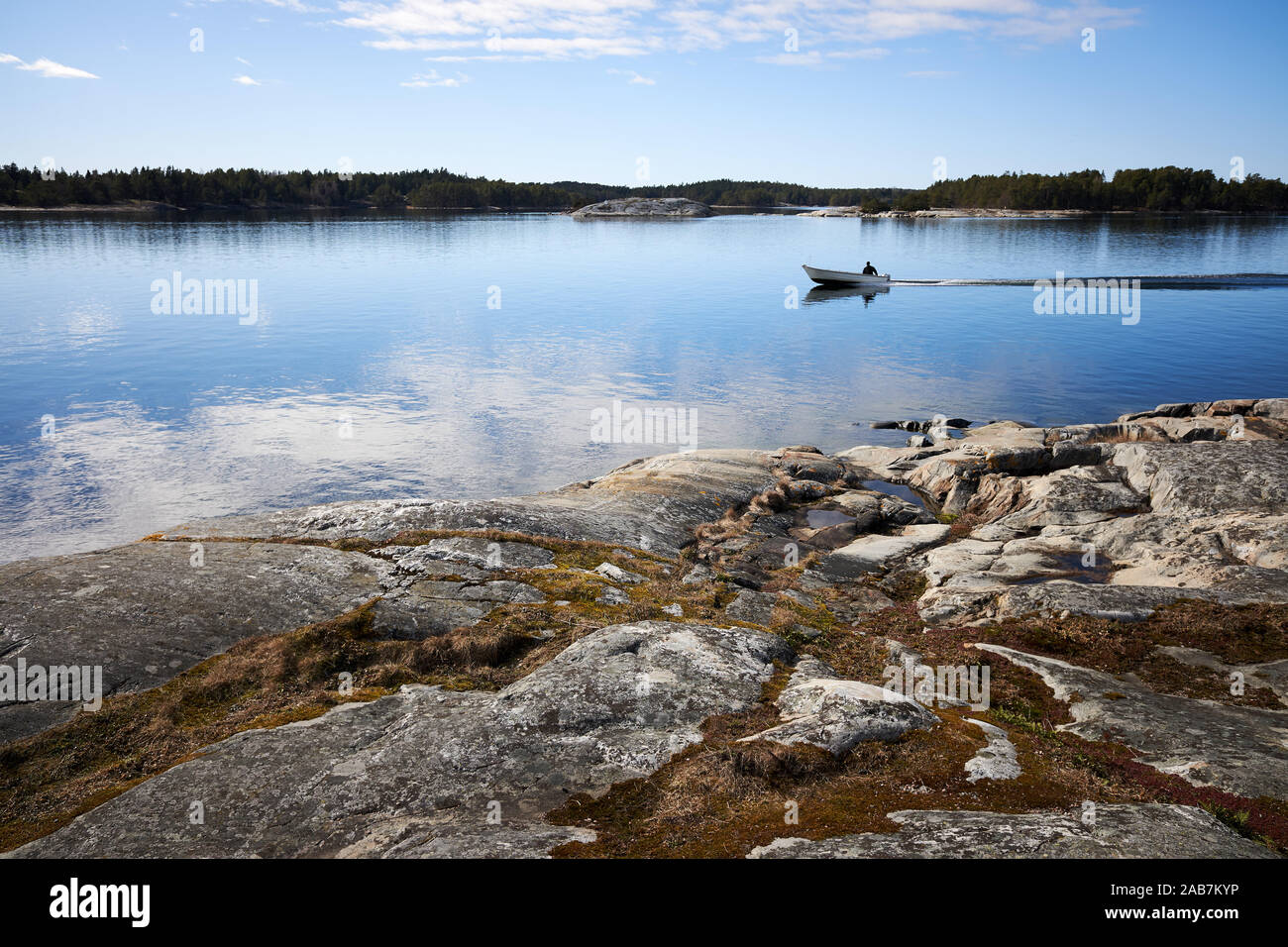 Small fishing boat on still sea water. Beautiful rocks on the shore of th Baltic Sea in Kassnäs, Kemiö island in Finland. Stock Photo