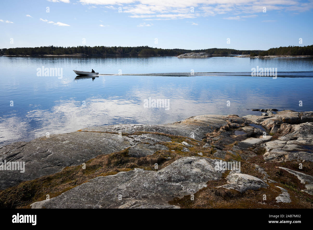 Small fishing boat on still sea water. Beautiful rocks on the shore of th Baltic Sea in Kassnäs, Kemiö island in Finland. Stock Photo