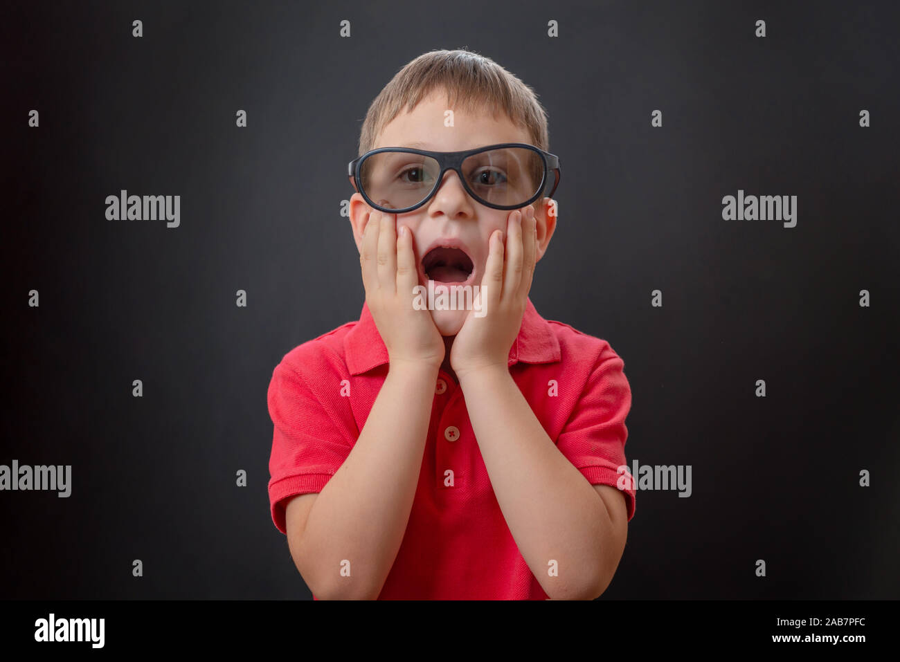 Surprised boy with open mouth and with hands on his face watching a movie with 3d glasses. Black background. Stock Photo