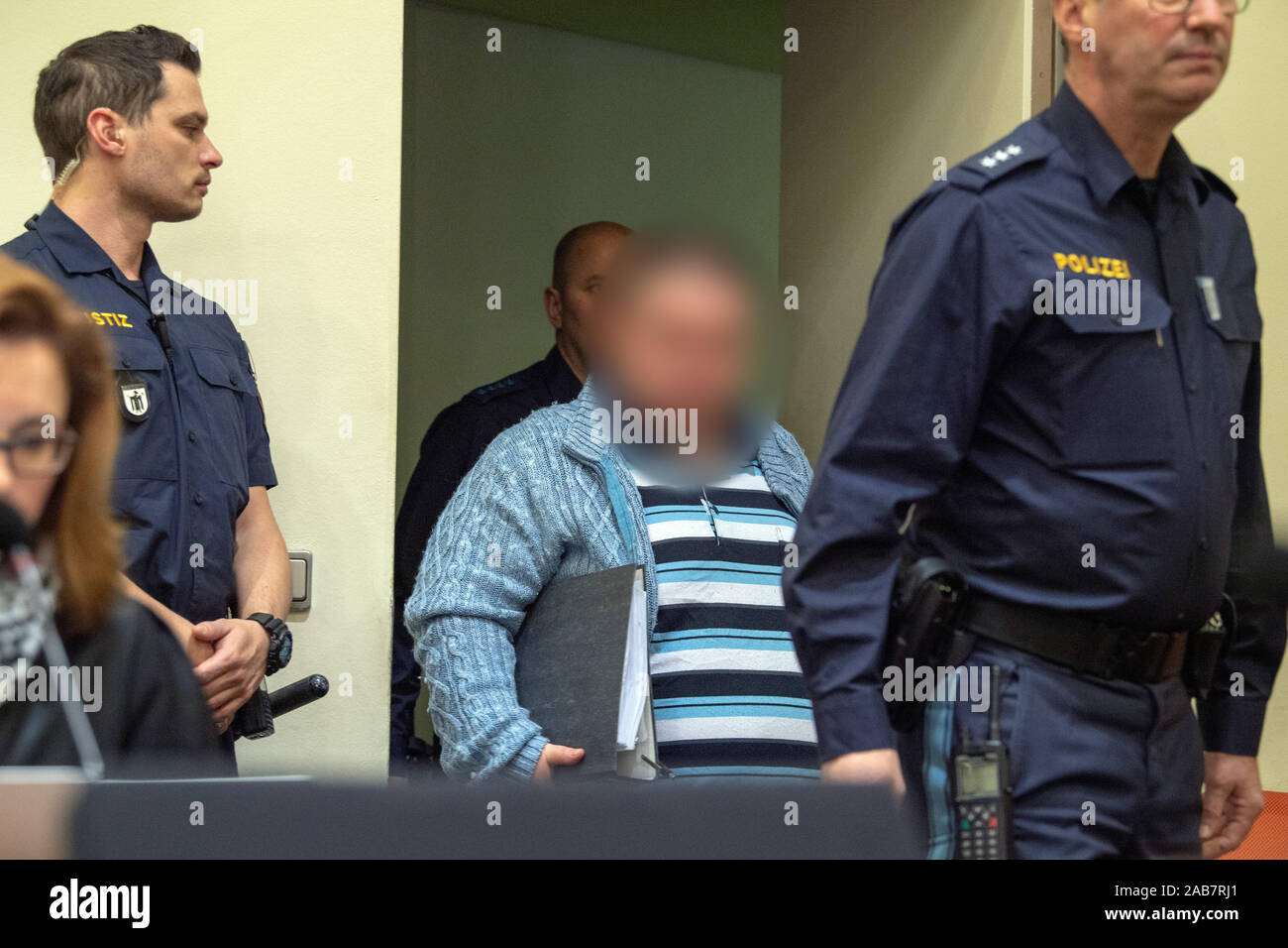 Munich, Germany. 26th Nov, 2019. The defendant (M) is taken to his place in court by police and judicial officers at the start of the trial. The auxiliary nurse is being tried for the murder of at least six patients. Credit: Peter Kneffel/dpa - ATTENTION: person(s) was/are pixelated for legal reasons/dpa/Alamy Live News Stock Photo