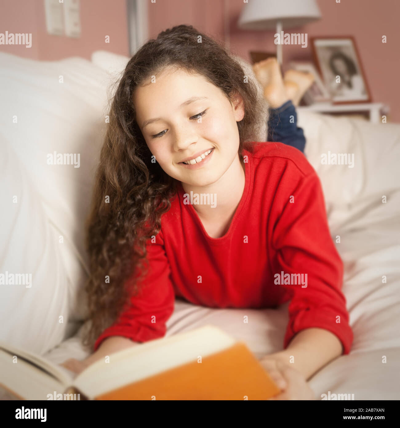 Ein junges Maedchen im roten Pullover mit einem dicken Buch in der Hand Stock Photo