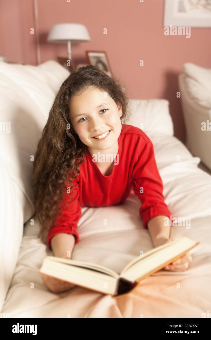 Ein junges Maedchen im roten Pullover mit einem dicken Buch in der Hand Stock Photo