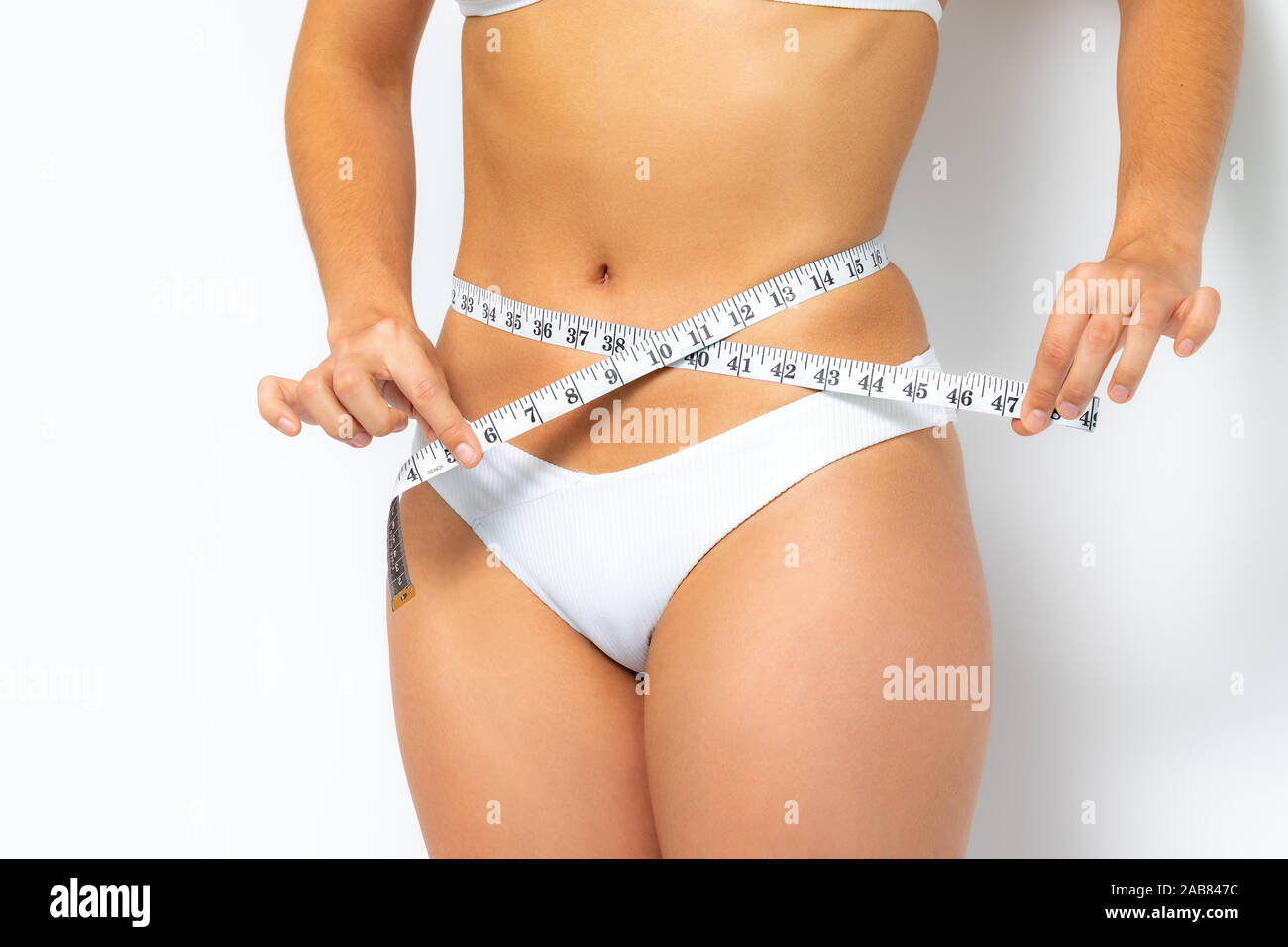Close up female waist in white bikini. Hands measuring waist with metric band. Stock Photo