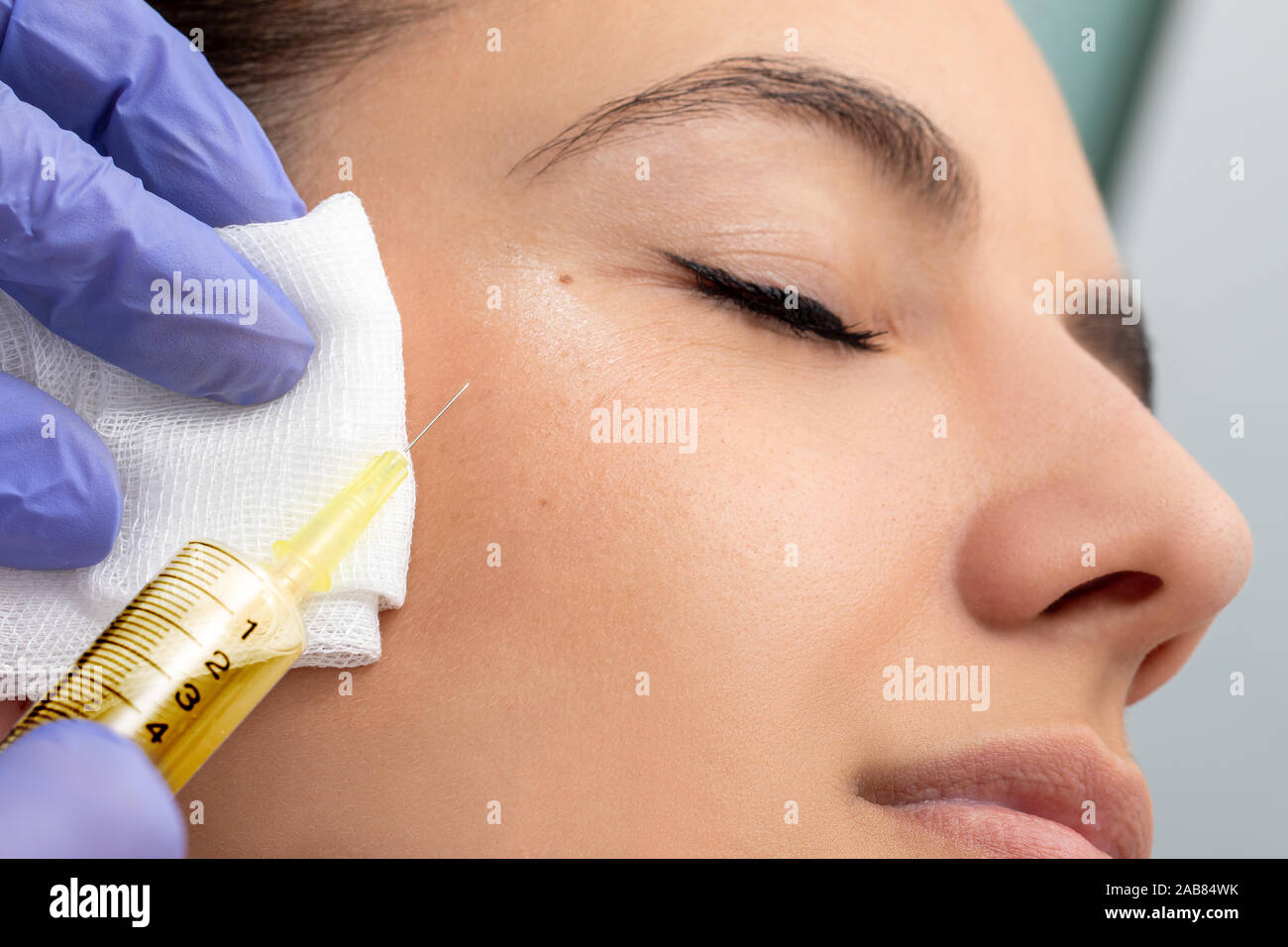 Macro close up of syringe with needle next to woman's face. Therapist doing cosmetic hormone treatment on girl. Stock Photo