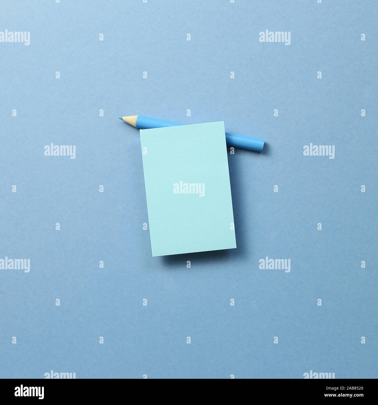 Blue memo note pad and blue colored pencil on blue background Stock Photo