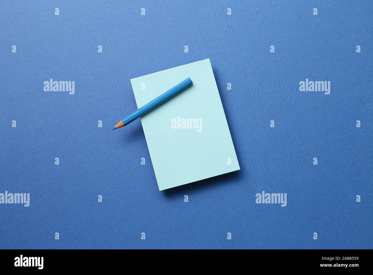 Blue memo note pad and blue colored pencil on blue background Stock Photo
