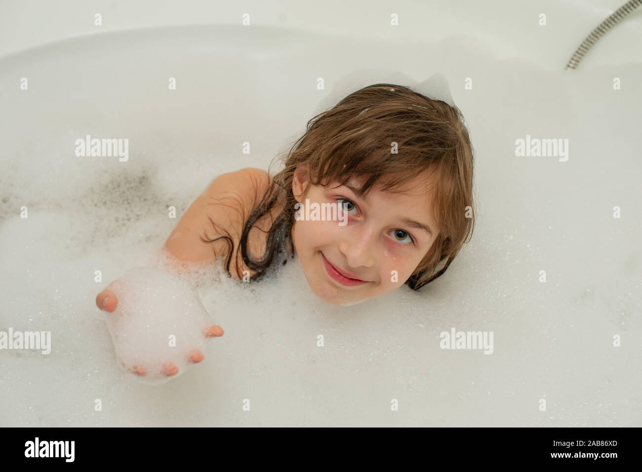 Young girl inside the bath. A little girl bathes in a bathtub with foam ...