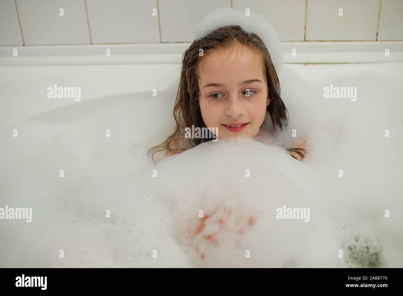 Young girl inside the bath. A little girl bathes in a bathtub with foam ...