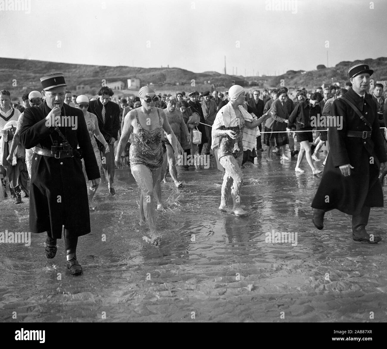 Flanked by gendarmes and followed by the crowd, competitors - covered by a thick layer of grease - walk down to the sea off Cap Gris-Nez, France, with Dover - and a £1,000  first prize - as their aim in the Cross-Channel swimming race. Stock Photo