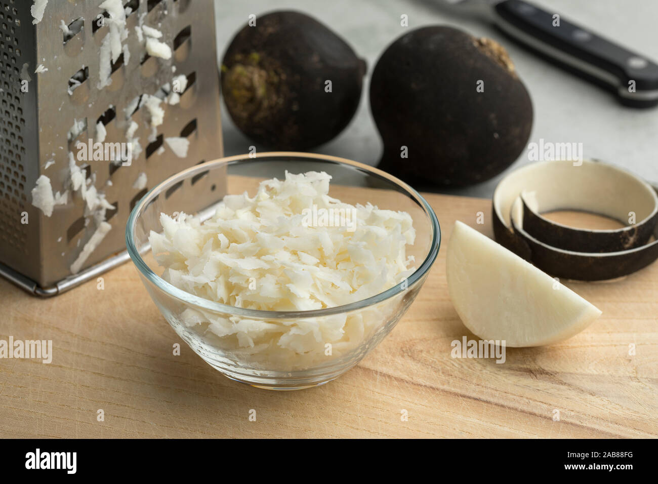 Glass bowl with grated black radish and whole radishes in the background Stock Photo