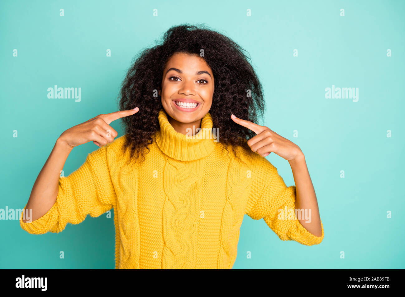 Photo of amazing dark skin curly lady indicating fingers on perfect condition teeth advertising dentist wear yellow knitted pullover isolated blue Stock Photo