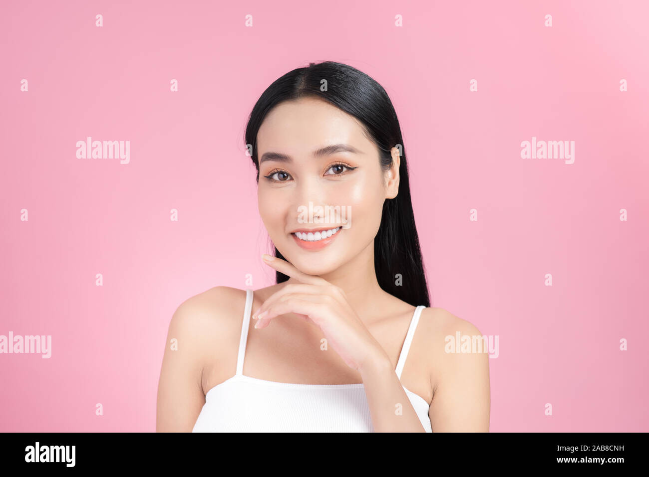 Beautiful young Asian girl touching her perfect skin on pink background ...