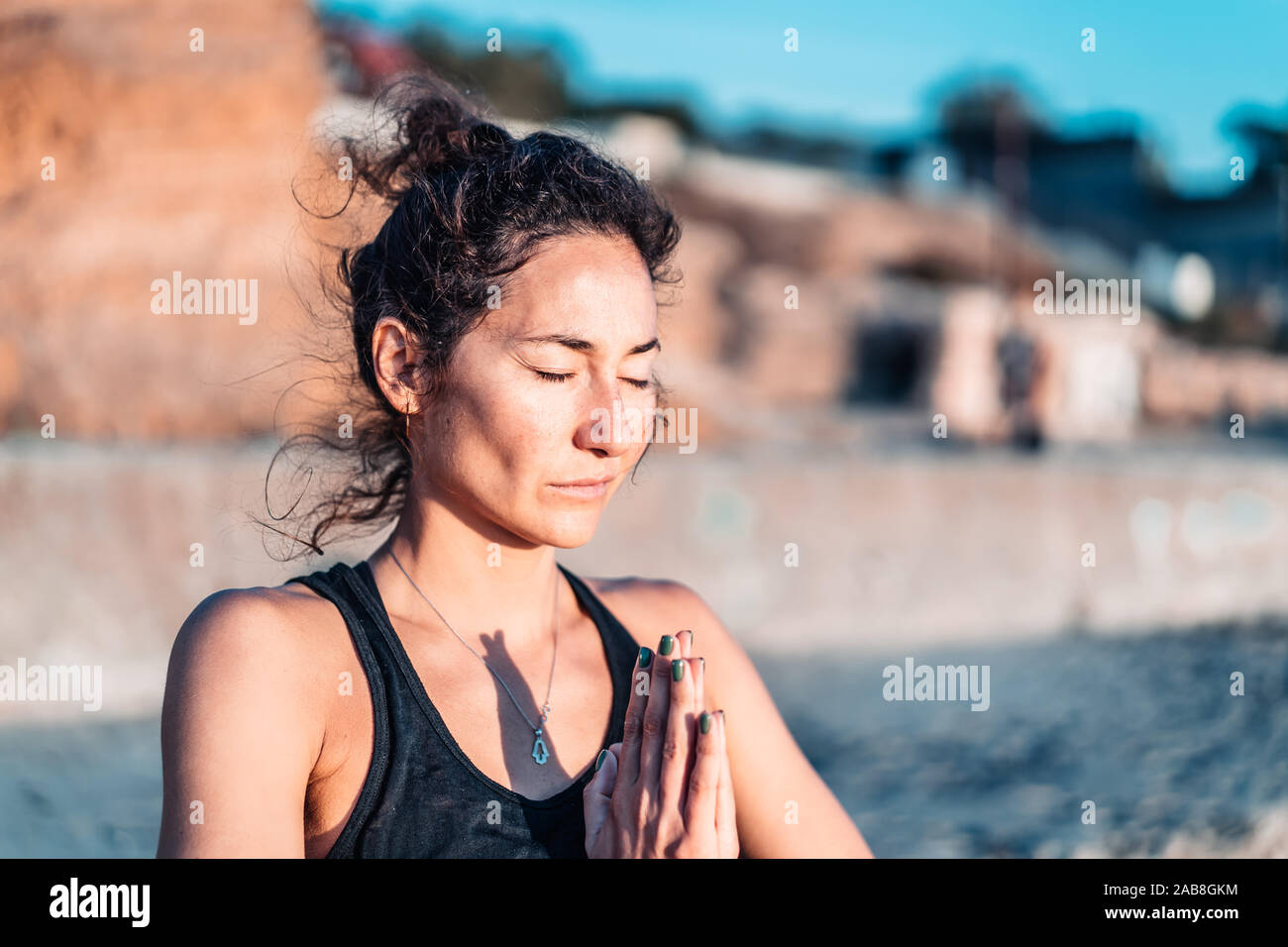 Pleasant woman makes greeting to the sun at sunrise on sea coast. Hands in namaste. Yoga, meditation, gratitude, healthy lifestyle concept. Stock Photo