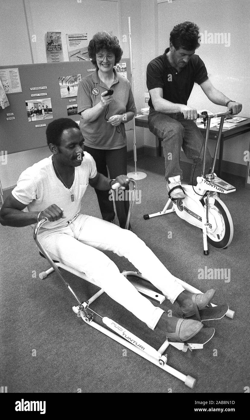 1980s, historical, healthly hearts, inside an office, staff using home gym kit, a rowing machine and an indoor exercise bike, inativive to improve mployees health, England, UK. Stock Photo