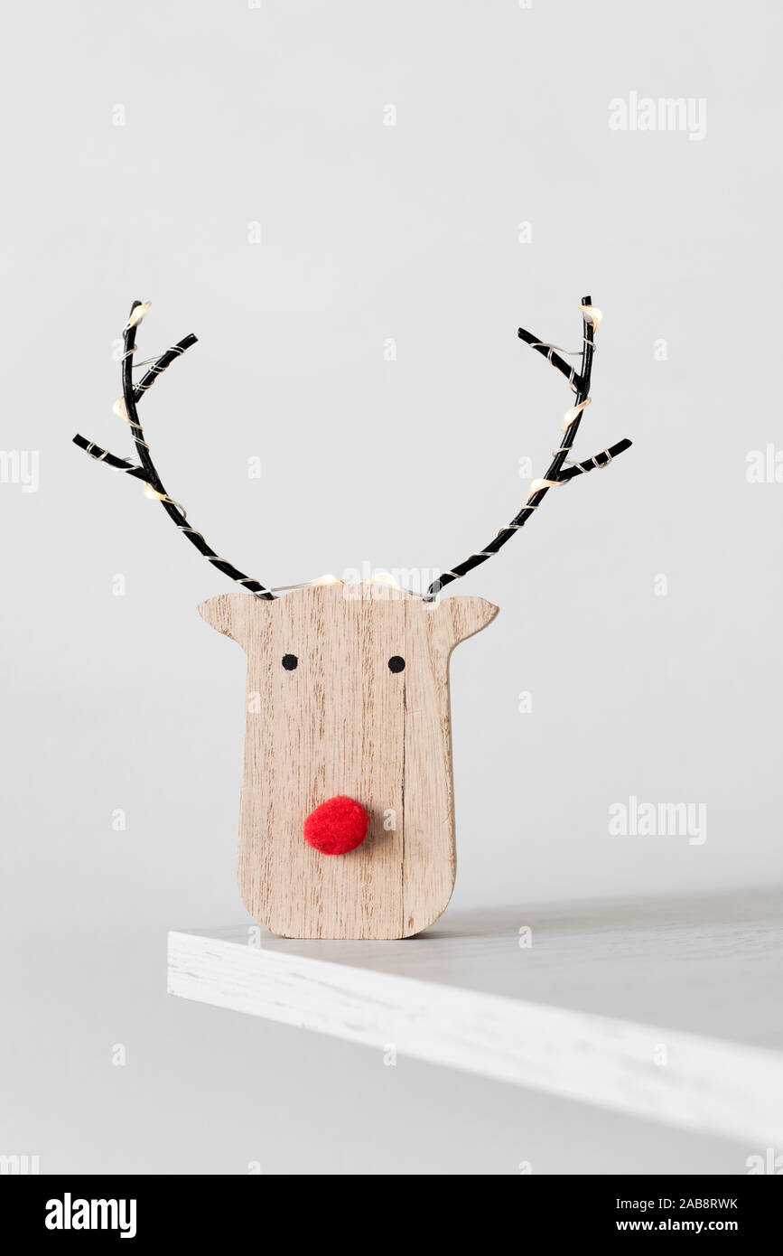 a funny wooden reindeer head, with a red nose, on a wooden shelf against an off-white background Stock Photo