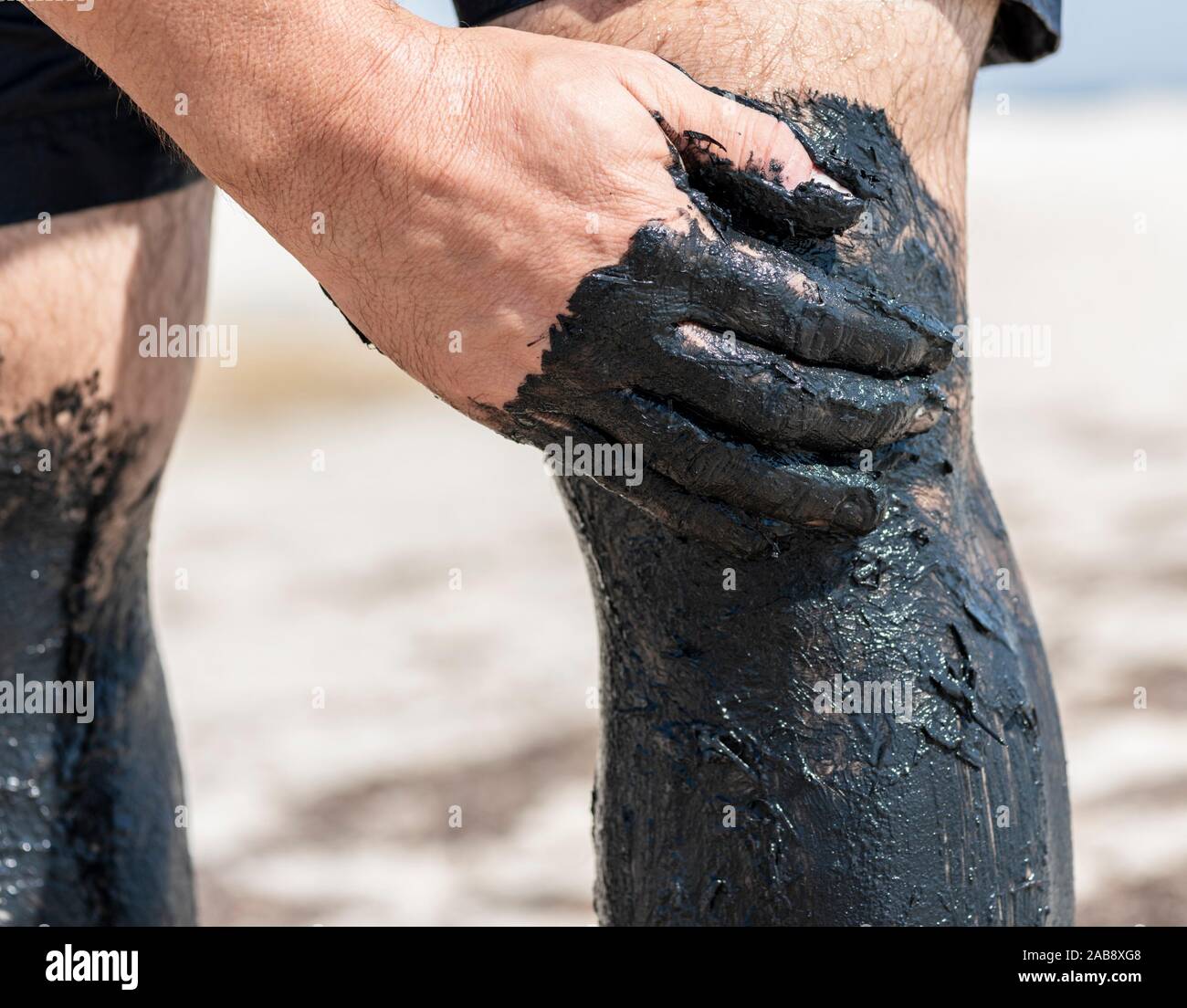 man's hand smears a leg with black mud, treatment with natural