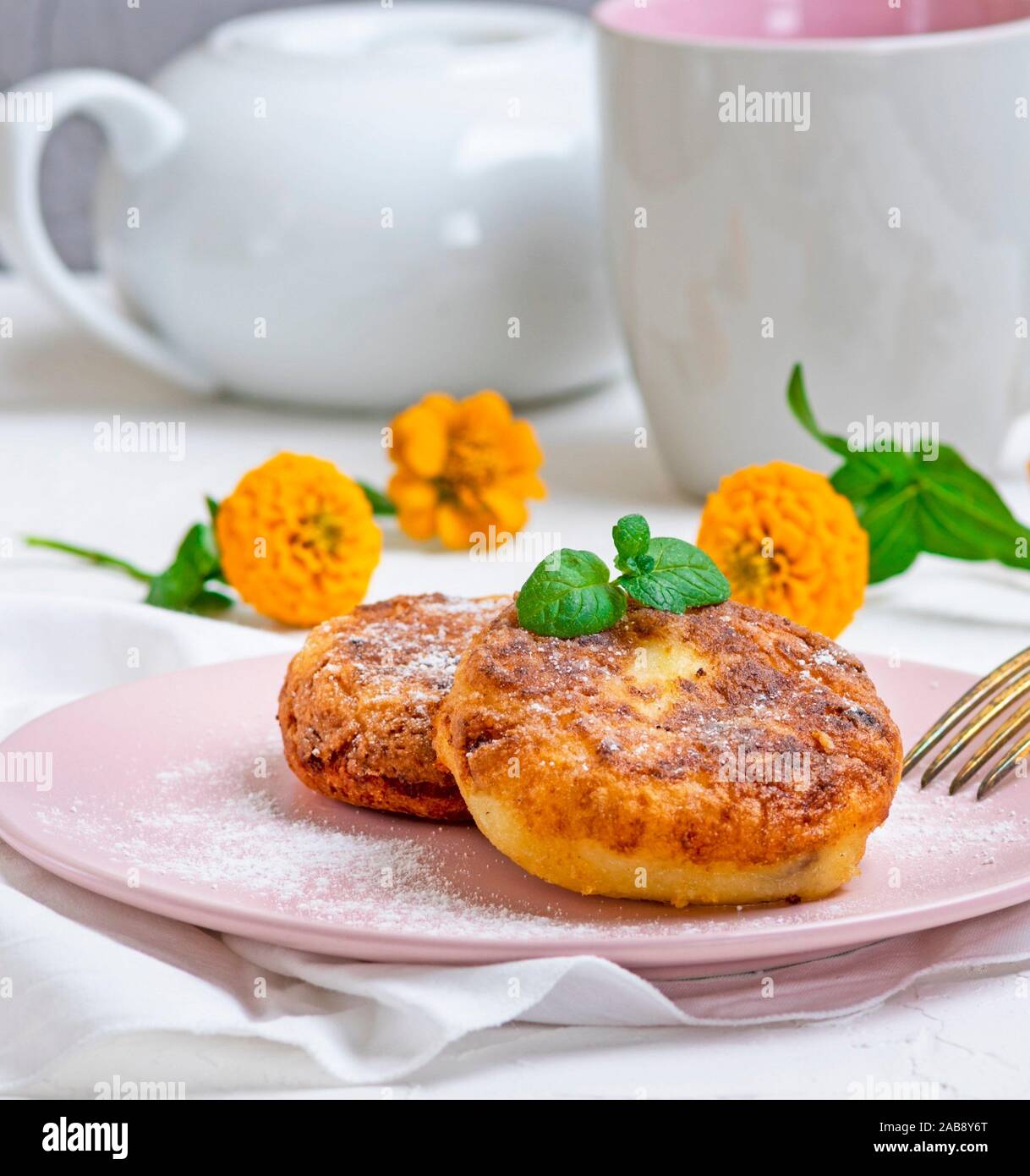 Cottage cheese pancakes on a pink plate, sprinkled with powdered sugar