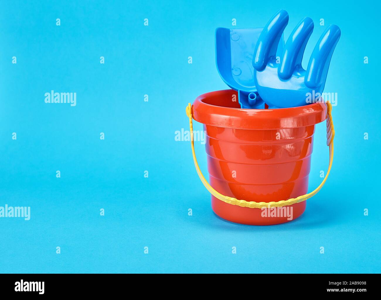 baby plastic red bucket and shovel with a rake on a blue background