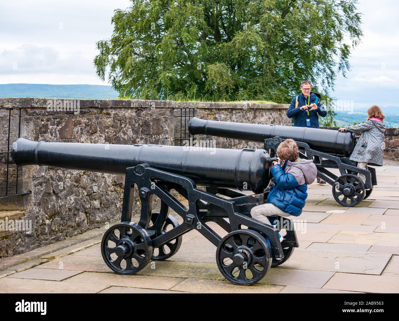 Family with father and children playing on old artillery cannons or guns on Grand Battery, Stirling Castle, Scotland, UK Stock Photo