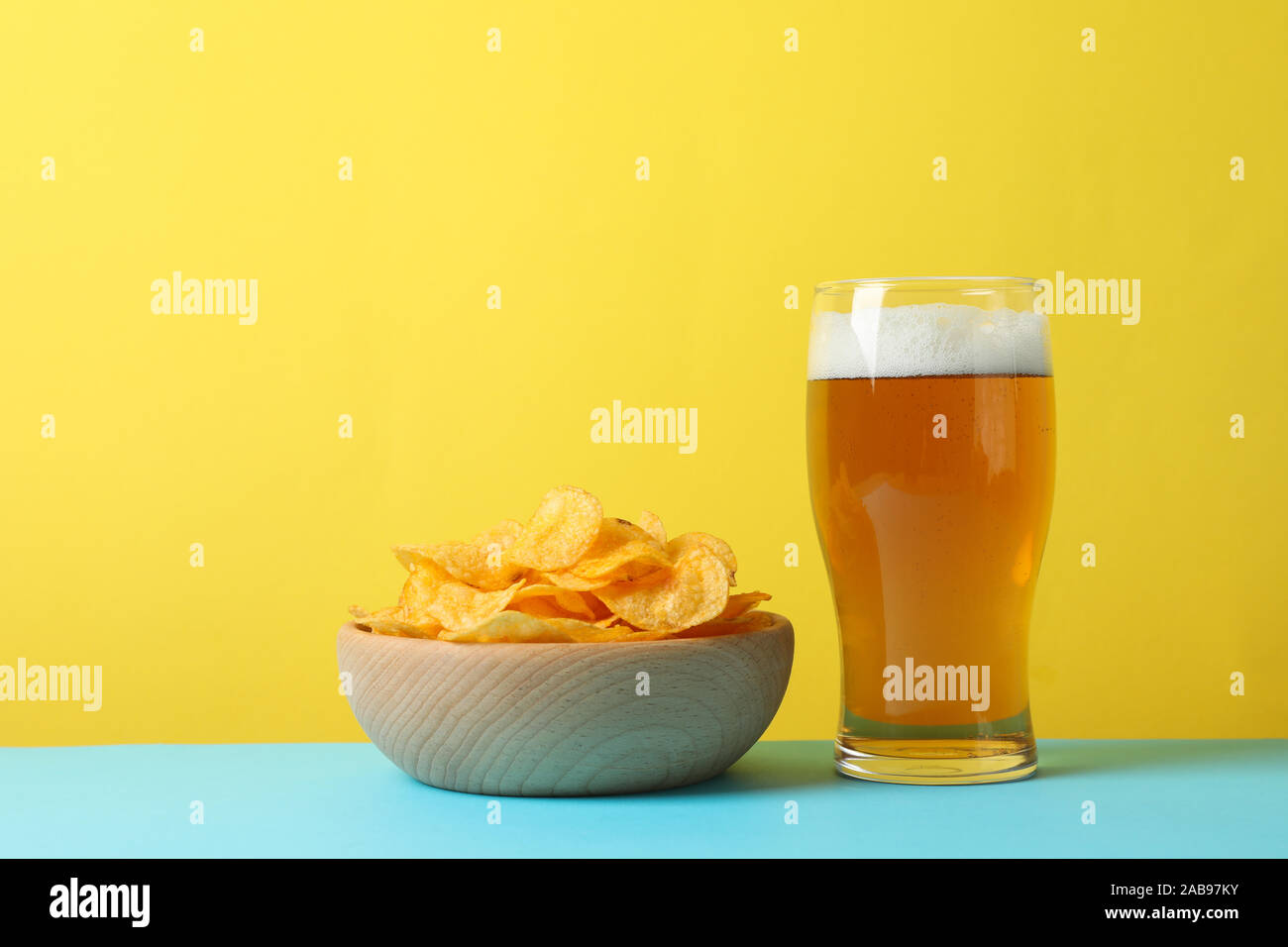 Potato chips in a bowl and glass of beer. Beer snacks on blue background against yellow background, space for text Stock Photo