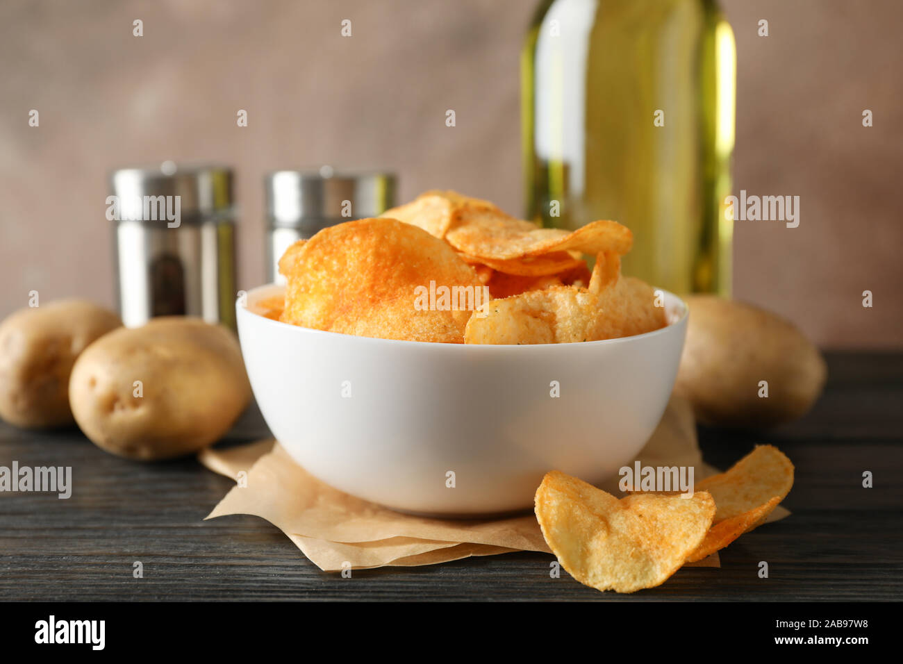 Potato chips in a bowl on craft paper. Potato, spice, olive oil on wooden background, space for text. Closeup Stock Photo