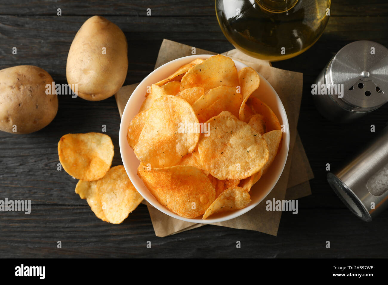 Potato chips in a bowl on craft paper. Potato, spice, olive oil on wooden background, closeup. Top view Stock Photo