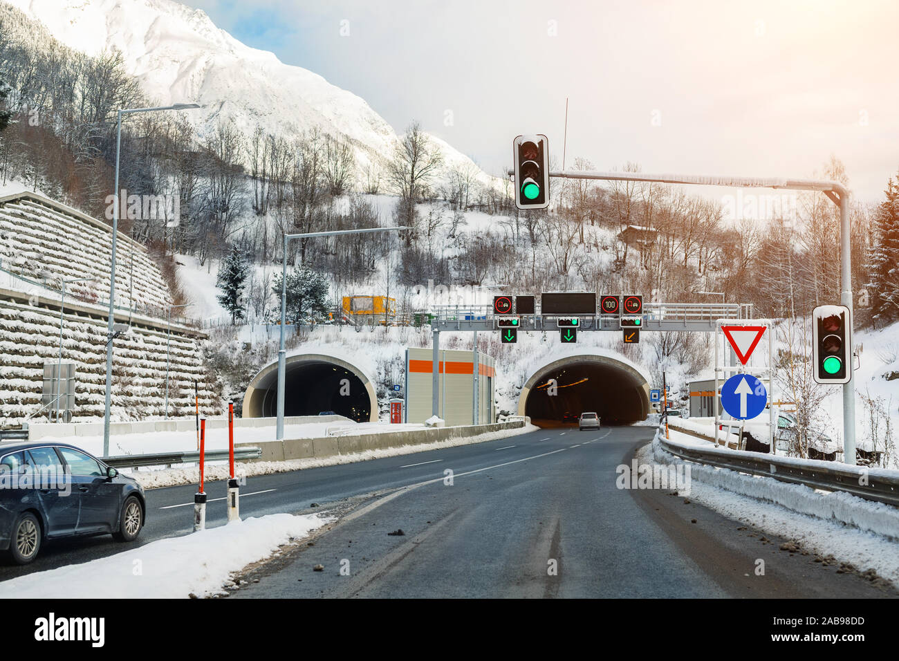 Winter alpine road landscape with tunnel, forest, mountains and blue sky on background at bright cold sunny day. Car trip family travel journey Stock Photo