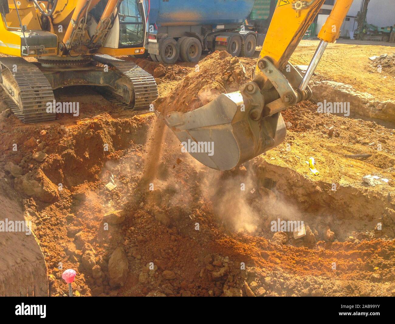 Excavator loading the ground plot at construction site. Dump truck waiting close. Stock Photo