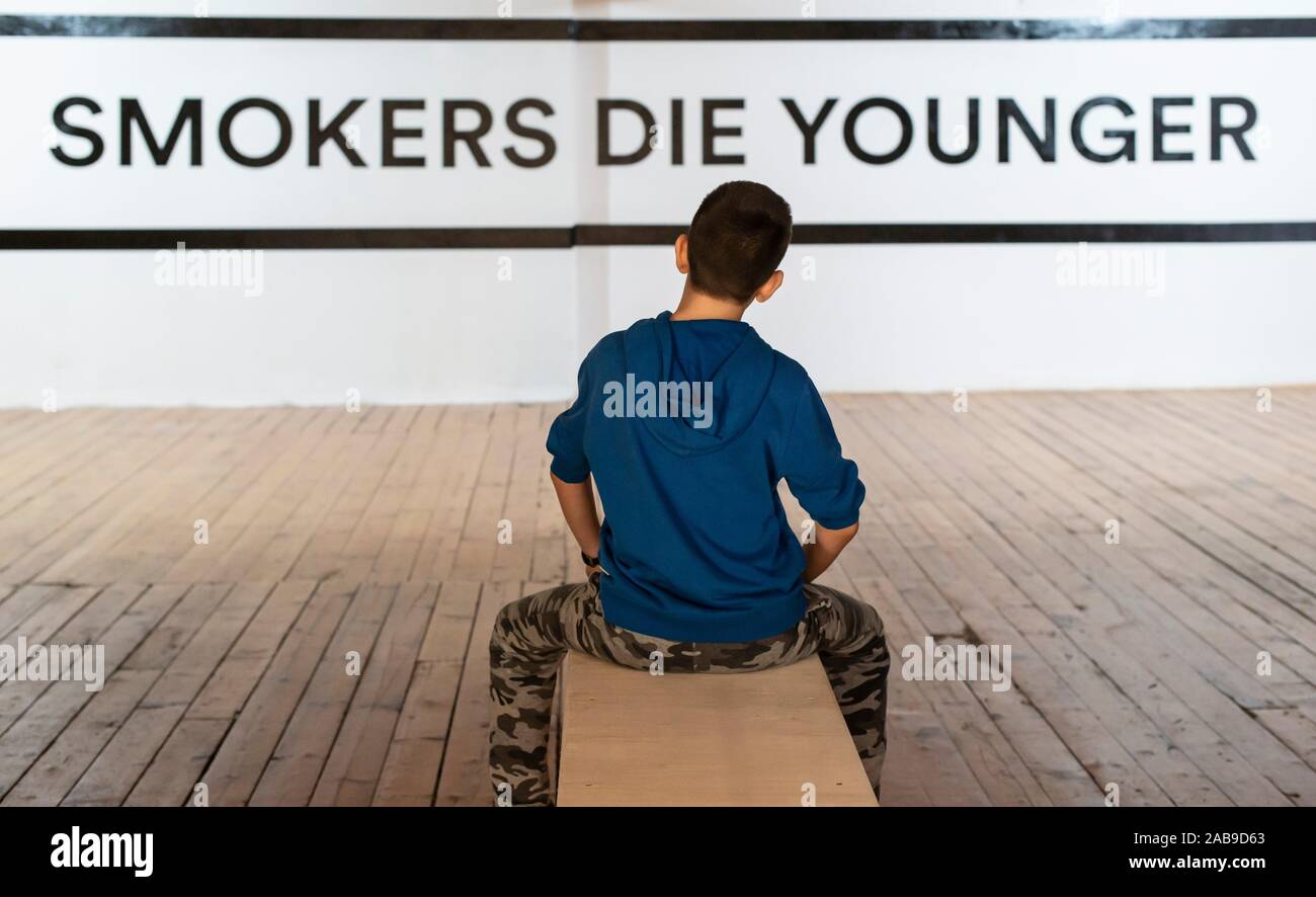 Teenager smoking and message on wall Smokers die younger. No smoking