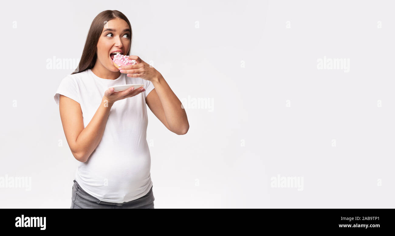 Expectant Lady Eating Donut Standing Over Gray Background, Panorama Stock Photo