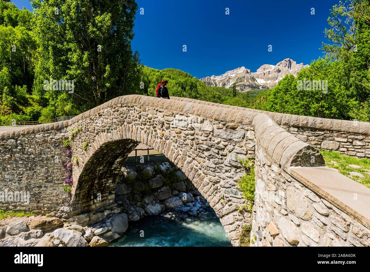 Young hiker crossing the old bridge of Bolática River, Panticosa, Tena Valley, Pyrenees (Huesca province, Aragón, Spain) Stock Photo