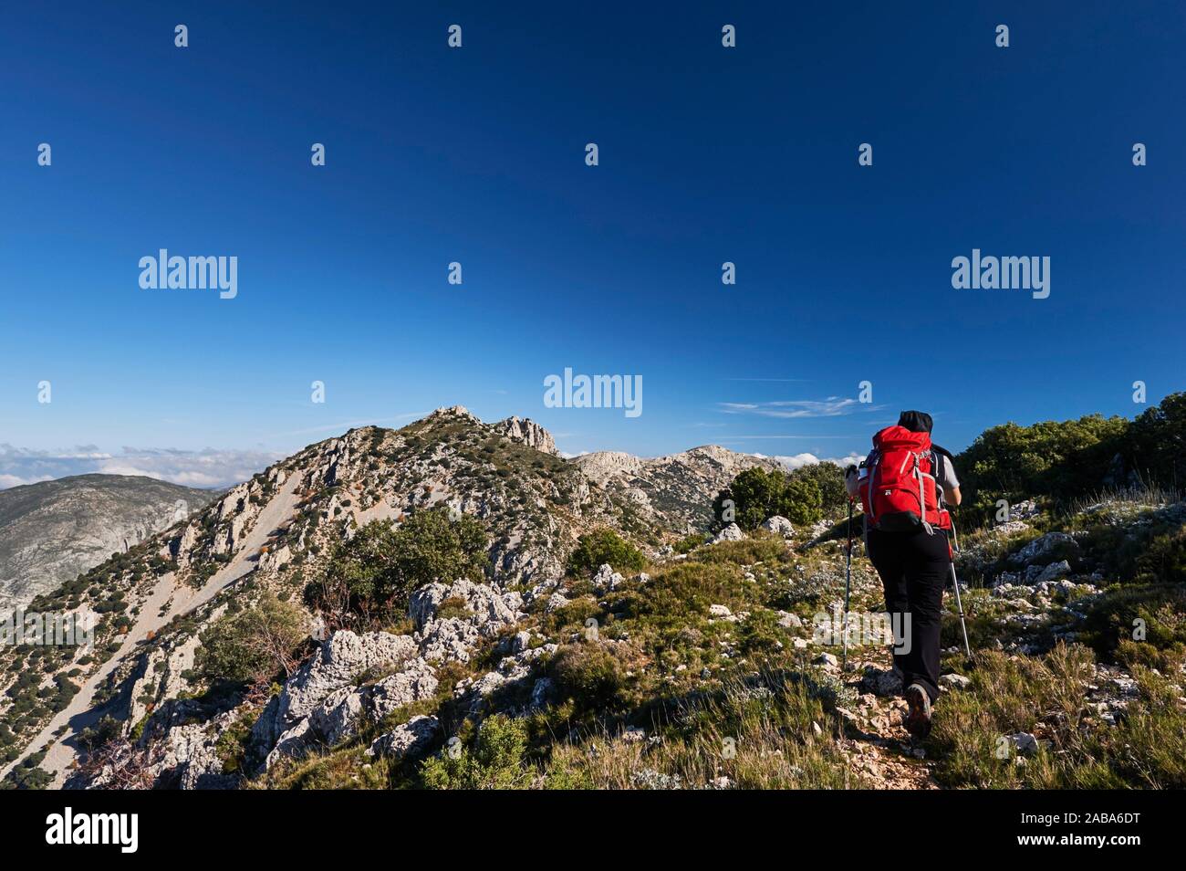 Woman with red backpack hiking near Pla de la Casa peak in Serrella mountain range, Confrides (province of Alicante, Valencian Community) Stock Photo