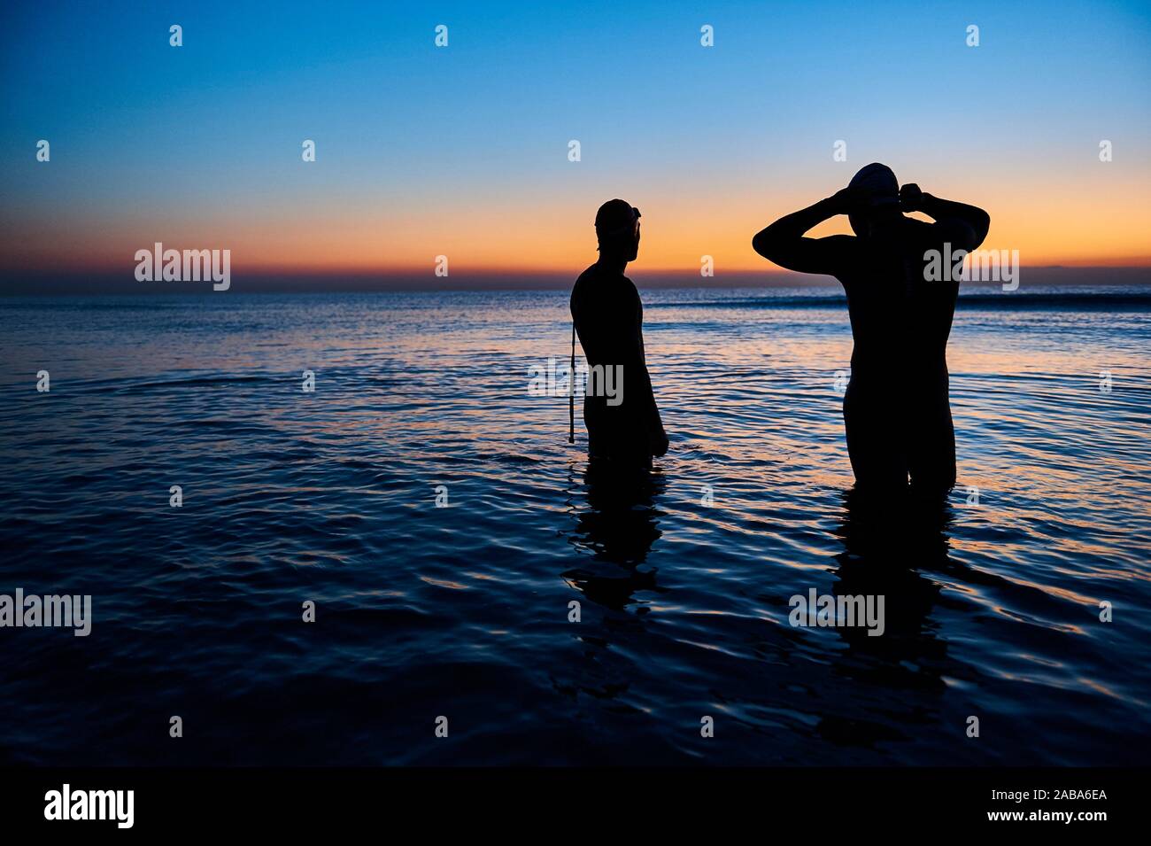 Two triathletes with wetsuit getting ready before triathlon training at sea Stock Photo