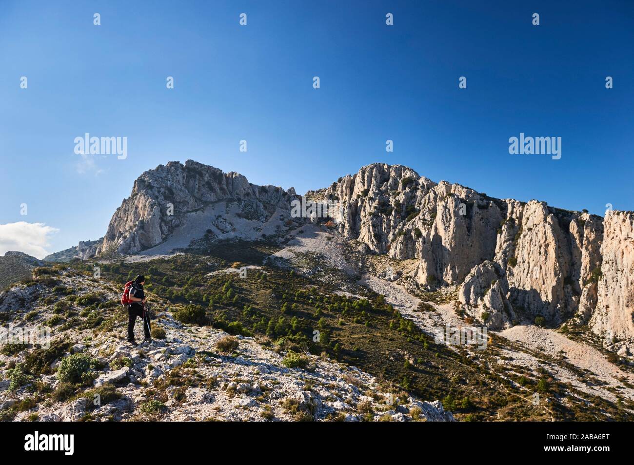 Woman with red backpack hiking near Pla de la Casa peak in Serrella mountain range, Confrides (province of Alicante, Valencian Community) Stock Photo